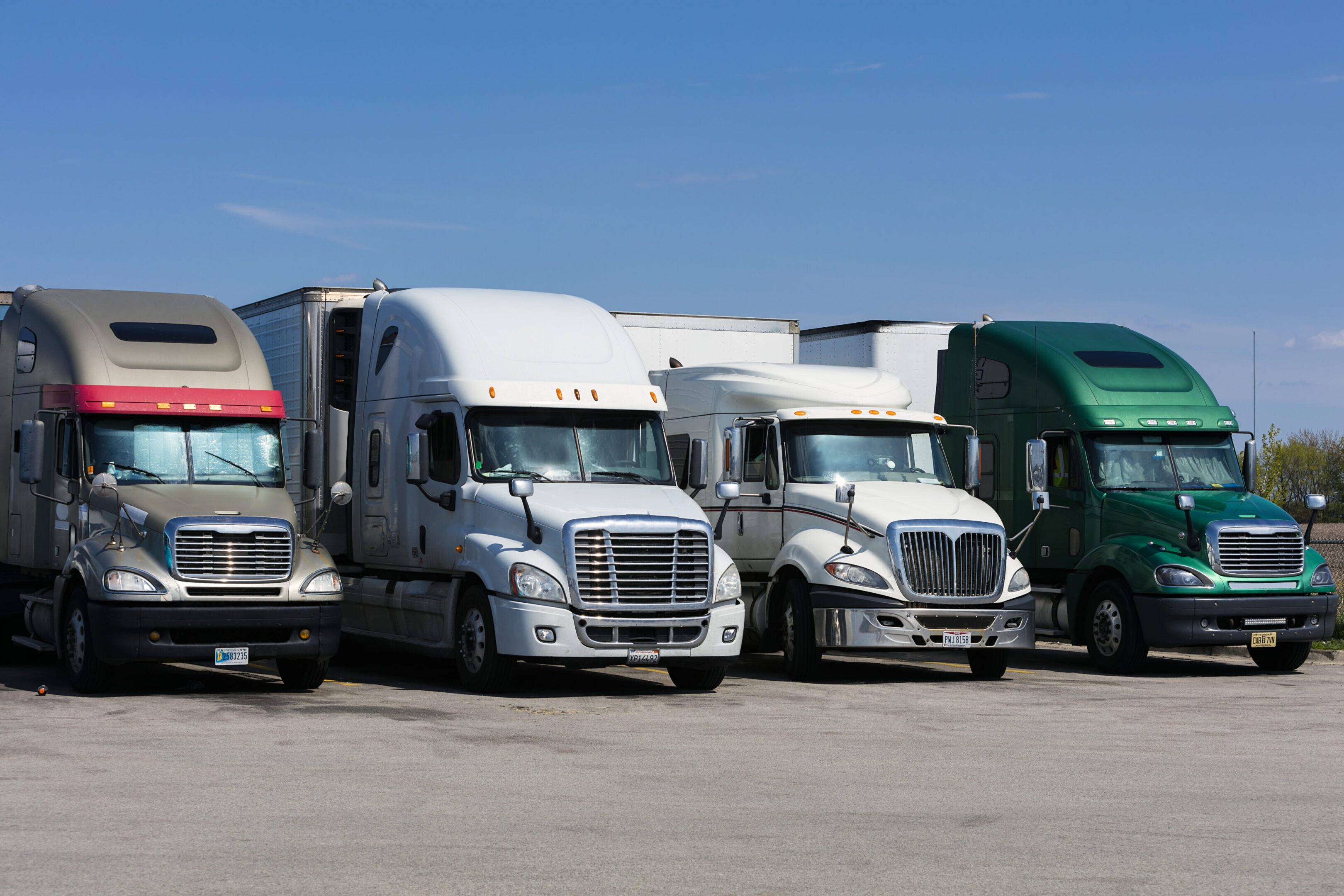 Four parked semi-trucks under clear sky.