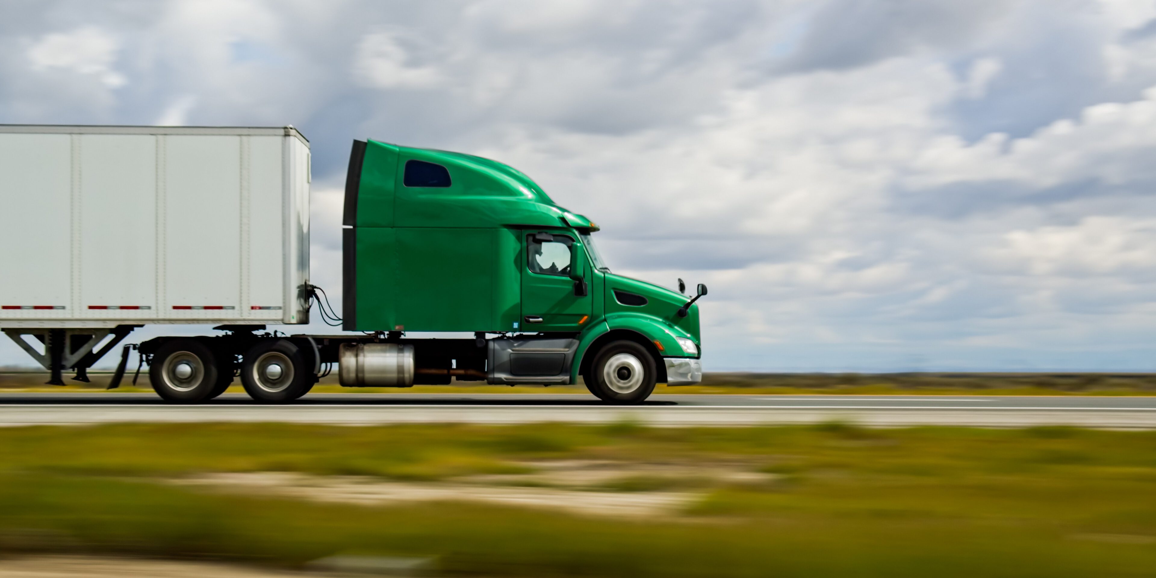 Green truck driving on open highway.